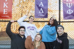 Five Ramapo Greek life students standing outside pointing to a few Greek banners