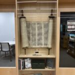 A Torah on display in a wooden cabinet between two glass doors.