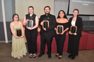 This picture has a group of five students holding leadership awards at the reception. 