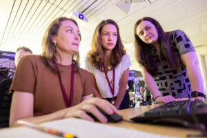 Three women gather around a computer to learn about investigative genetic genealogy in the Ramapo College IGG summer bootcamp program.