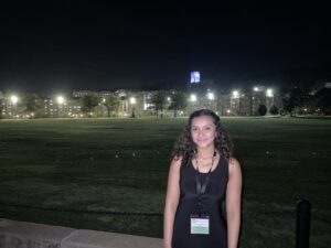 Stefanie Viera '25 stands on the West Point campus at night, academic buildings illuminated behind her.