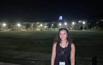 Stefanie Viera '25 stands on the West Point campus at night, academic buildings illuminated behind her.