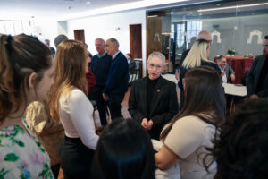 Susan Vallario faces towards us in the center of the photo, while she speaks to presidential scholars who are in the foreground, facing her. Other guests for the reception to announce the gift are in the background chatting with each other.