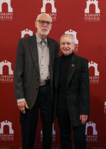 Nick and Susan Vallario stand together for a photo in front of a maroon and white Ramapo College step and repeat