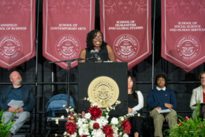 Author Victoria Christopher Murray speaks at the lectern addressing the Class of 2028. Maroon banners hang in the background on stage.