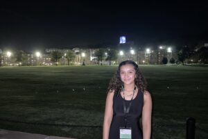 Stefanie Viera '25 stands on the West Point campus at night, academic buildings illuminated behind her.